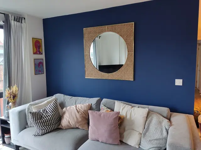 Round rattan mirror mounted on a navy living-room wall